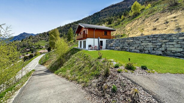 Una casa de madera de dos pisos con un muro de piedra y un camino pavimentado que conduce a ella.