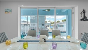 Comedor con vistas a una piscina y una playa, con una mesa dispuesta con platos, vasos y salero y pimentero.