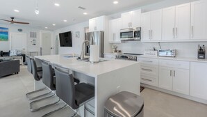 Una cocina moderna con armarios blancos, electrodomésticos de acero inoxidable y una isla central con taburetes de bar.