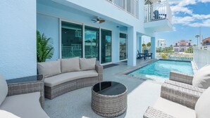 Zona junto a la piscina con un sofá, sillas de mimbre y una piscina.