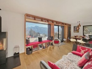 Ein modernes Wohnzimmer mit Kamin, Essbereich und großem Fenster mit Bergblick.