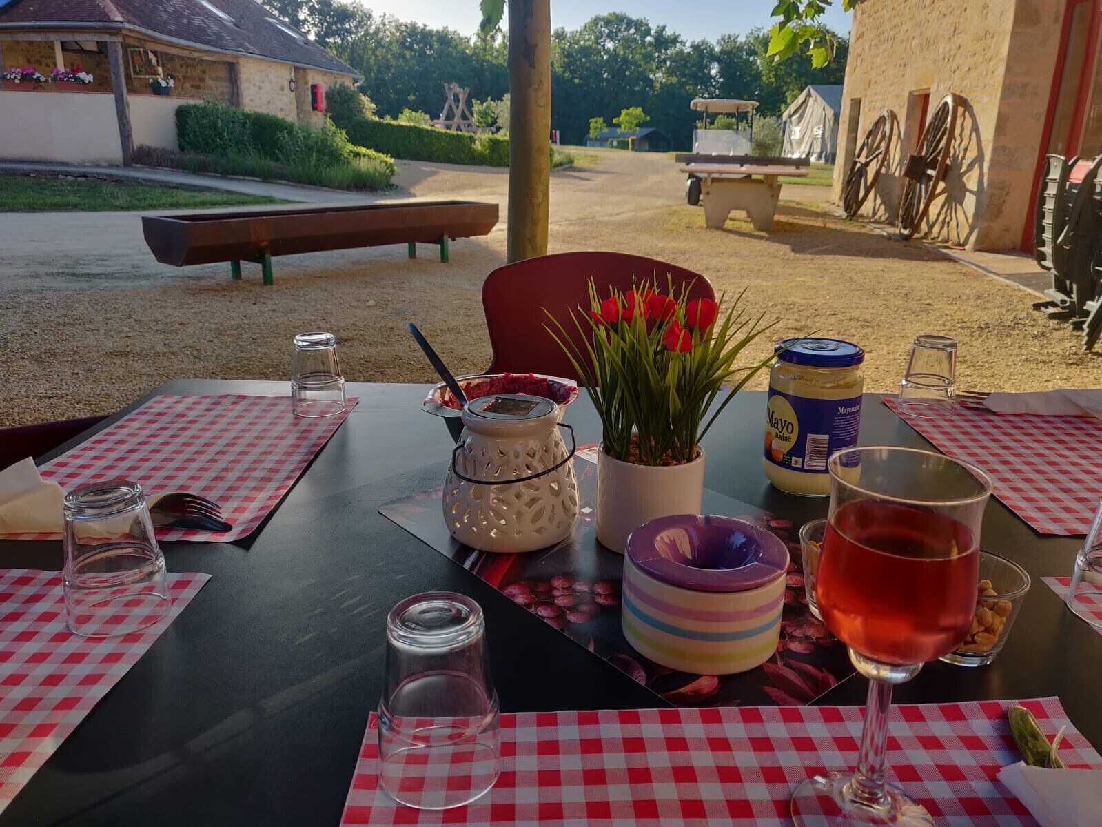 An outdoor dining area with tables set for two, featuring checkered tablecloths, a variety of dishes, and a bottle of wine.