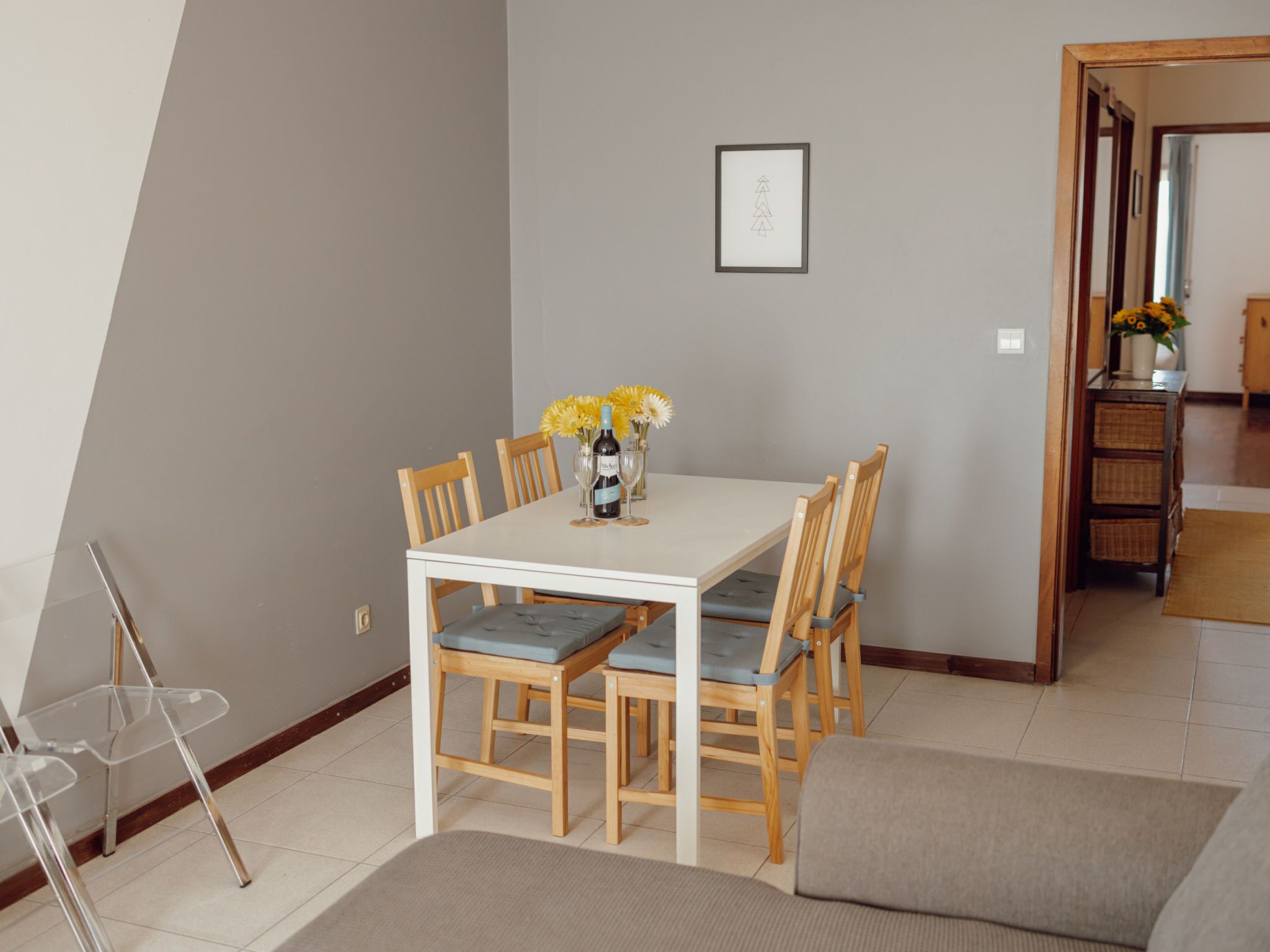Un comedor con una mesa blanca, seis sillas de madera y un jarrón con flores amarillas.