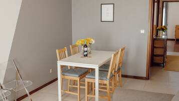 Un comedor con una mesa blanca, seis sillas de madera y un jarrón con flores amarillas.