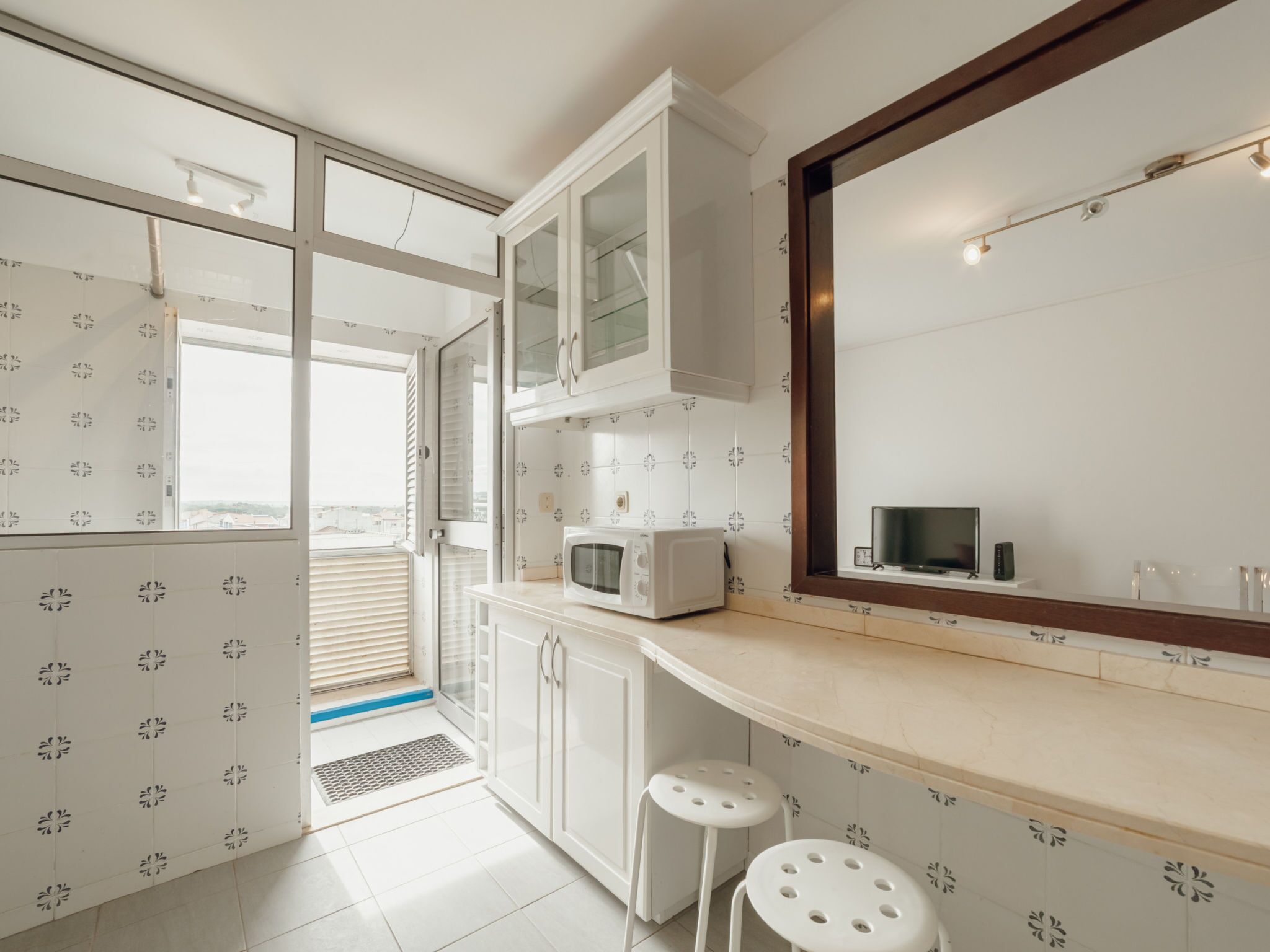 Una cocina moderna con armarios blancos, microondas y un espejo grande.