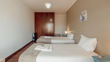 Habitación de hotel con dos camas, un armario de madera, una mesita de noche con lámpara y una obra de arte en la pared.