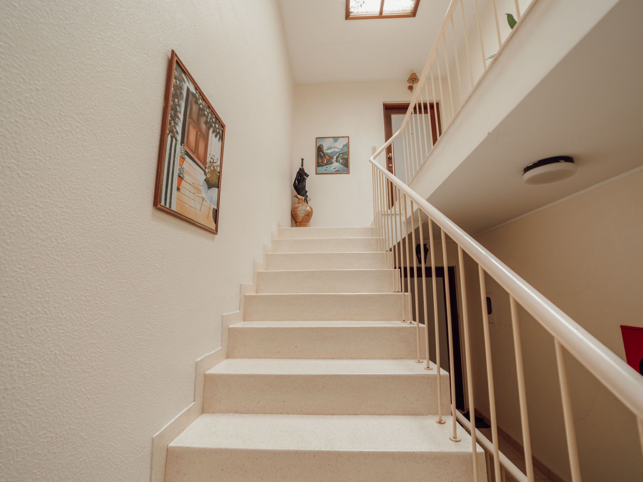 Un escalier avec des rampes blanches et des marches de couleur beige menant à un palier.
