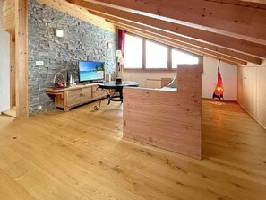 Ein Zimmer mit Steinwand, Holzbalken, einem Fernseher, einem Holzschrank und einer roten Pendelleuchte.