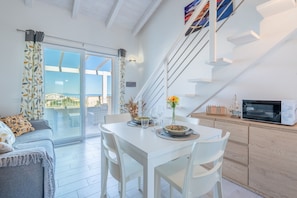 A modern kitchen with white cabinetry, a dining table, and a microwave. - Affittimoderni Castelsardo - Panorama (Castelsardo)