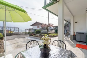 Une terrasse avec une table, des chaises, un parasol vert et une vue sur une maison et un jardin.