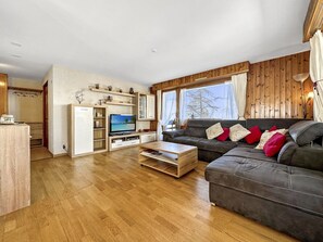 Ein modernes Wohnzimmer mit Holzboden, einer Sofagarnitur, einem Fernseher und Einbauschränken.