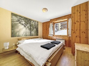 Ein Schlafzimmer mit einem großen Bett, Holzwänden, einem Fenster mit Blick auf einen verschneiten Berg und einem Baumgemälde.