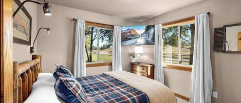 Un dormitorio con cama, mesita de noche, lámpara, un cuadro y ventana con cortinas.