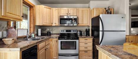Cocina compacta con armarios de madera, electrodomésticos de acero inoxidable y lavavajillas.