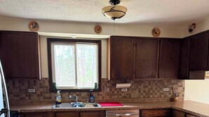 A kitchen with dark wooden cabinets, a tiled backsplash, a window, and a dishwasher. - Hayward Riverside Rental (Hayward)