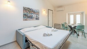 Ein Schlafzimmer mit Bett, Esstisch mit Stühlen, einem Bild an der Wand und einer Klimaanlage.