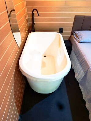 A small bathroom with a bathtub, a toilet, and a bed.
