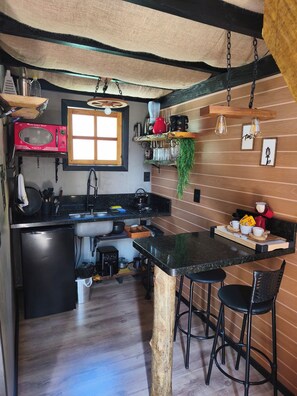 A compact kitchen with a microwave, sink, and bar stools.