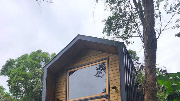 A wooden cabin with a balcony, a large window, and a staircase leading up to it.