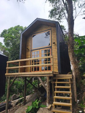 Una cabaña de madera con un balcón, un ventanal grande y una escalera que lleva hacia él.