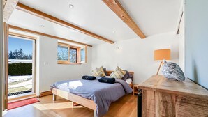 Quarto com uma cama grande, vigas de madeira, uma janela e uma mesa de cabeceira.