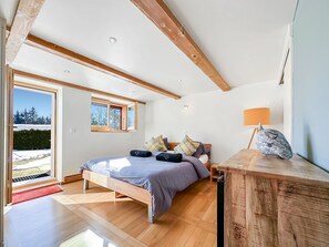 Ein Schlafzimmer mit einem großen Bett, Holzbalken, einem Fenster und einem Nachttisch.