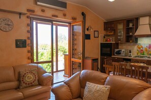 Ein Wohnzimmer mit einer Couch, ein Essbereich mit Tisch und Stühlen sowie eine Küche mit Geräten.