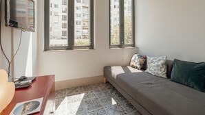 A small, well-lit room with a bed, a TV mounted on the wall, and a window with a view of a building. - Apartment  by Interhome (Porto)