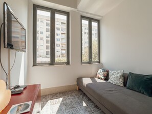 A small, well-lit room with a bed, a TV mounted on the wall, and a window with a view of a building. - Apartment  by Interhome (Porto)