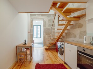 A compact kitchen with wooden flooring, a red rug, a washing machine, and a coffee maker. - Apartment  by Interhome (Porto)