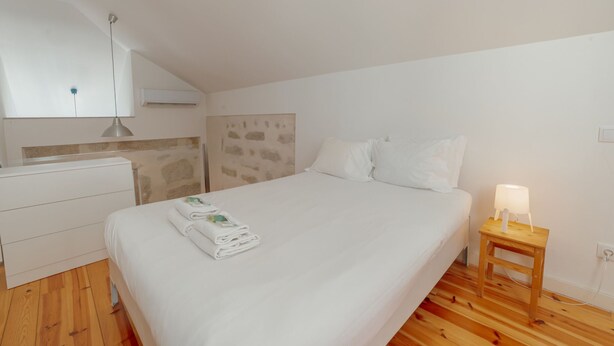 A bedroom with a bed, a wooden nightstand, a white dresser, and a stone-patterned wall. - Apartment  by Interhome (Porto)