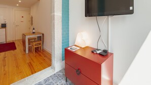 A hotel room with a flat-screen TV mounted on the wall, a wooden desk with a chair, a red dresser, and a tiled floor. - Apartment  by Interhome (Porto)