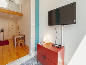 A hotel room with a flat-screen TV mounted on the wall, a wooden desk with a chair, a red dresser, and a tiled floor. - Apartment  by Interhome (Porto)