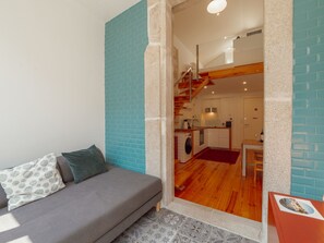 Una sala de estar moderna con un sofá gris, una pared de acento roja y vistas a una zona de cocina con una escalera de madera.