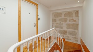A staircase with a wooden handrail leading to a room with a white door and a stone wall. - Apartment  by Interhome (Porto)