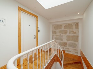 A staircase with a wooden handrail leading to a room with a white door and a stone wall. - Apartment  by Interhome (Porto)
