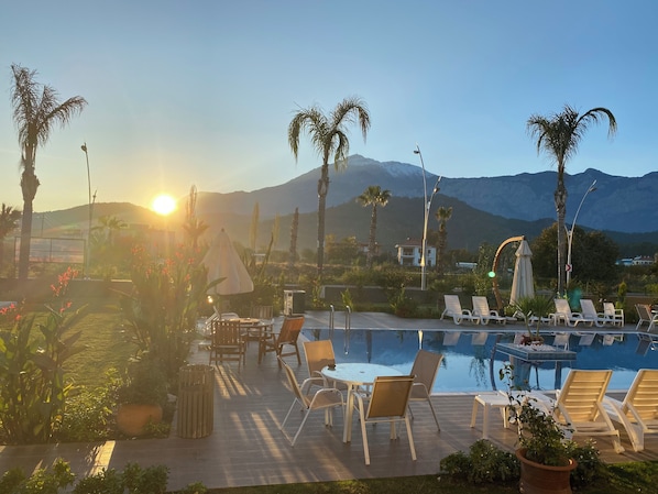 Ein Poolbereich mit Liegestühlen, einem Tisch und Blick auf Berge.