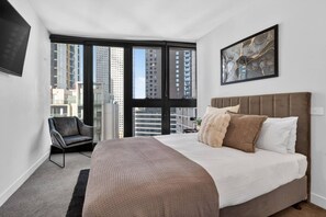 A modern hotel room with a large bed, a chair, a flat-screen TV, and a city view through large windows. - Luxury Sky-High Stay: Bay & Lake Views | Southbank (Southbank)