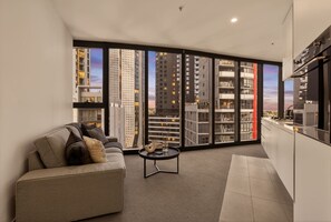 A modern living room with a sofa, a coffee table, and a view of tall buildings. - Luxury Sky-High Stay: Bay & Lake Views | Southbank (Southbank)