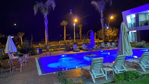A nighttime pool area with lounge chairs, umbrellas, and palm trees. - Mandalina Apartments A4 (Kemer)
