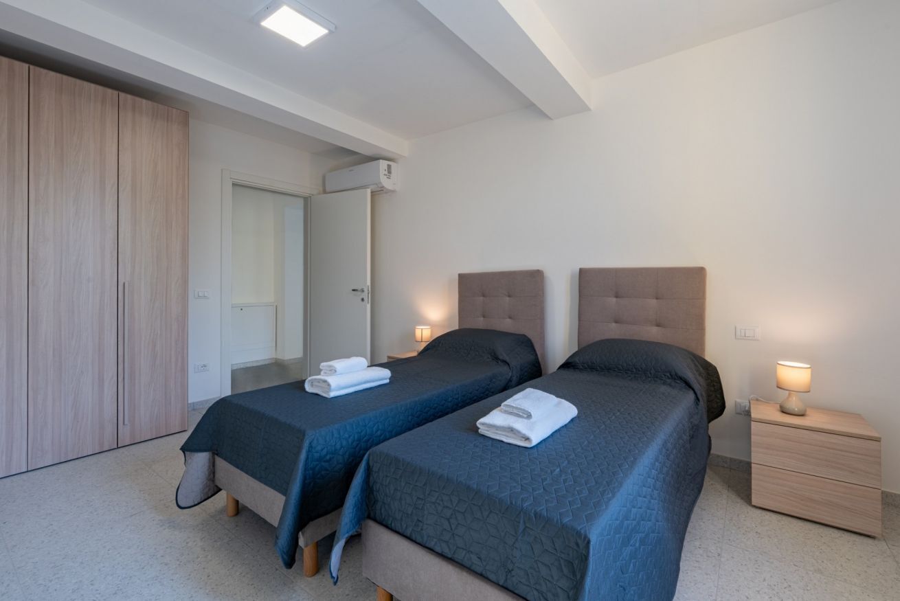 A bedroom with two beds, a wardrobe, a bedside table with a lamp, and a ceiling light.