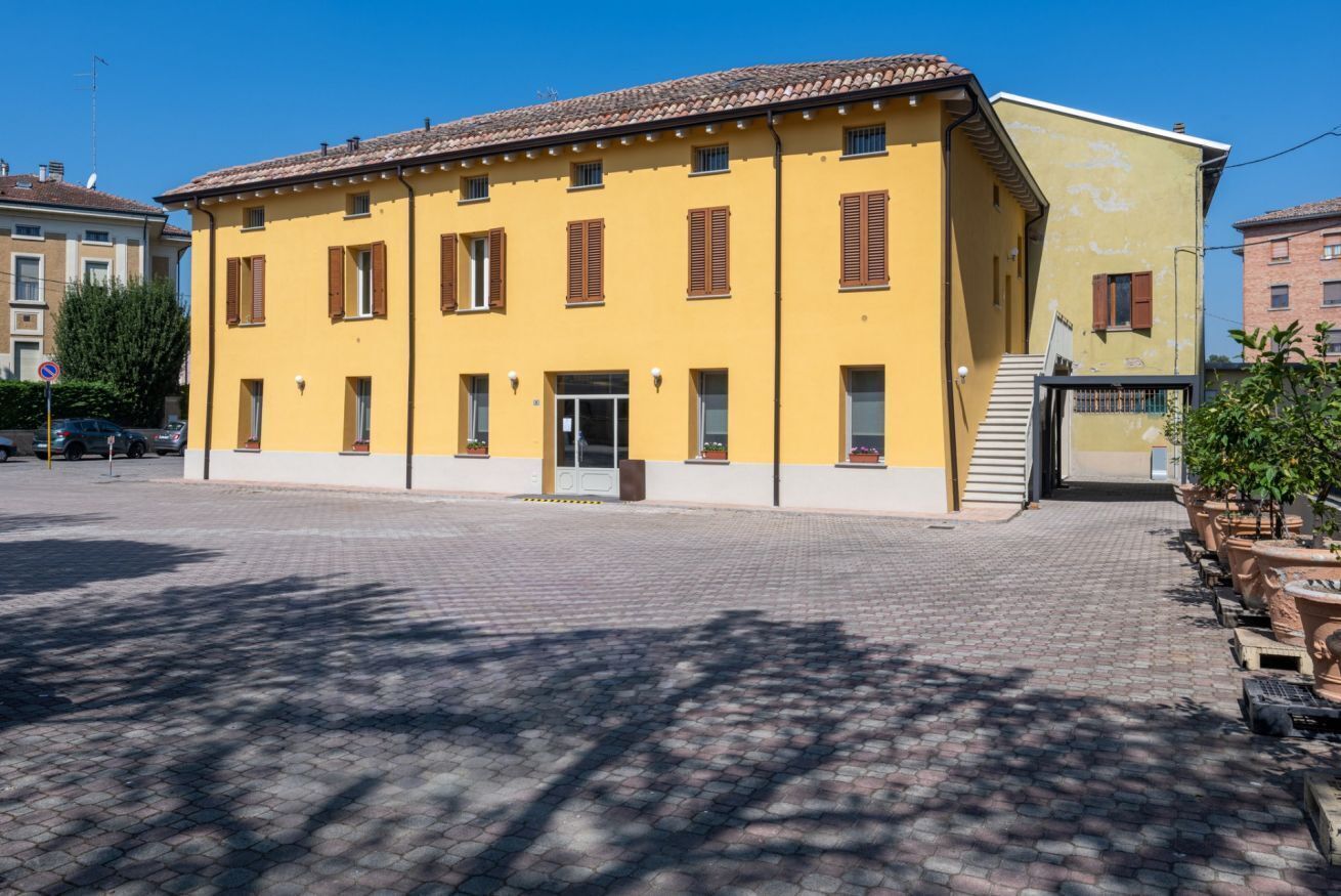 A yellow building with multiple windows and a door, surrounded by a paved area.