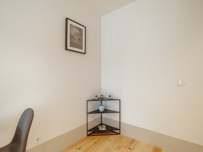 Ein Raumeck mit einem gerahmten Bild an der Wand, einem kleinen schwarzen Regal mit Dekorationen und einem Holzstuhl.
