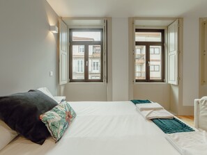 A bedroom with a bed, two windows, and a view of buildings outside. - Apartment  by Interhome (Porto)
