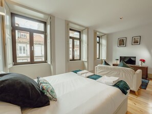 Et hotelværelse med seng, fjernsyn, skrivebord og vindue med udsigt til bygninger.