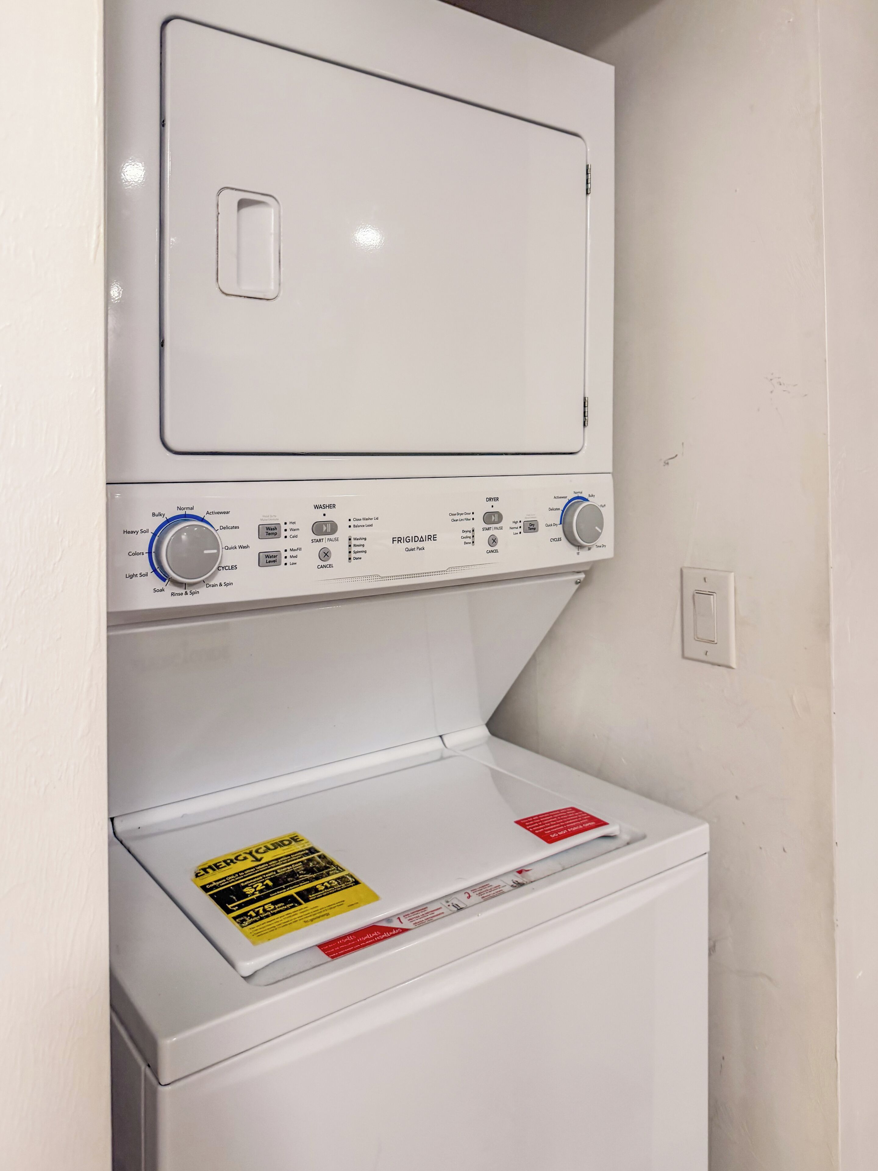 A front-loading washing machine with a control panel, a detergent dispenser, and a warning label.