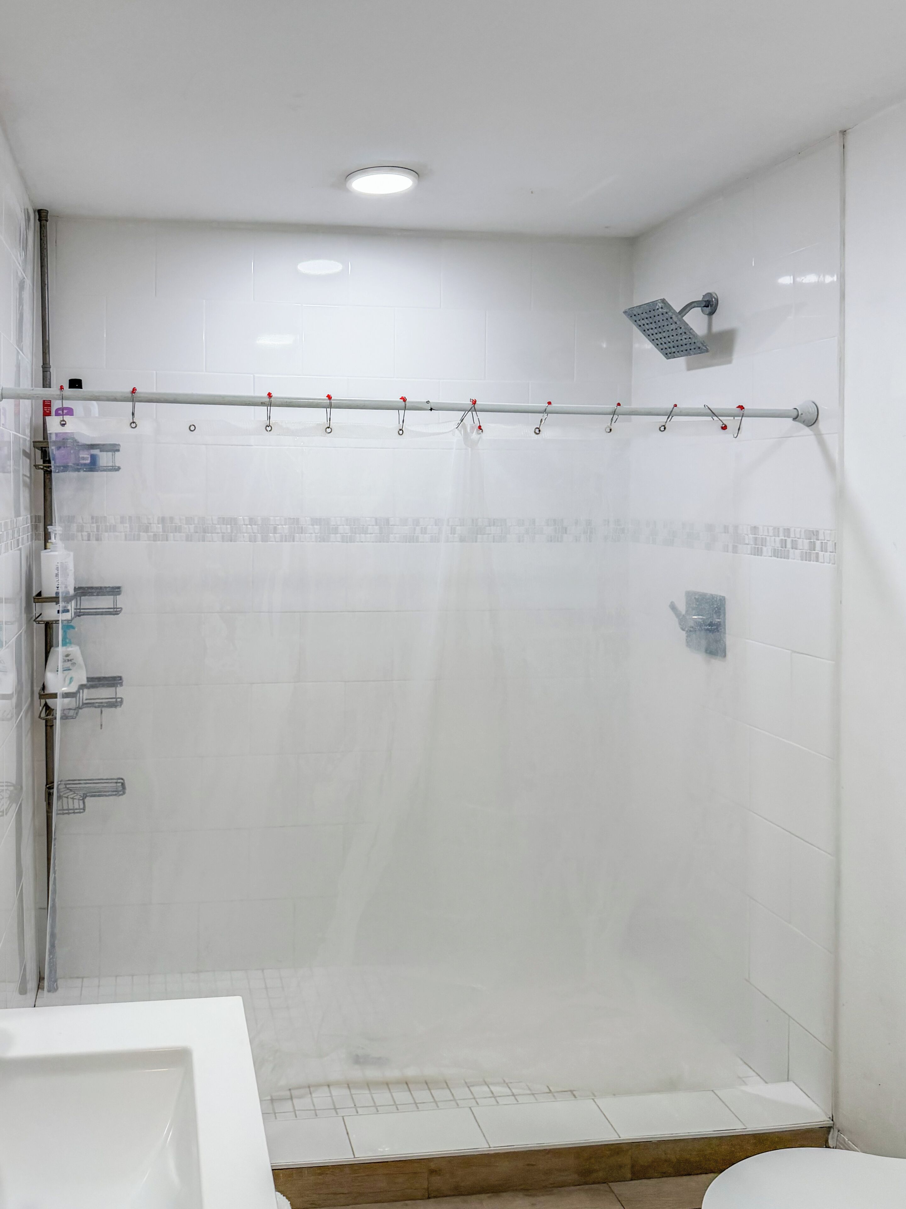 A bathroom with a shower, tiled walls, a ceiling light, and a showerhead.