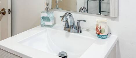 Un baño con un lavamanos blanco, un espejo, un perchero para toallas y un dispensador de jabón.