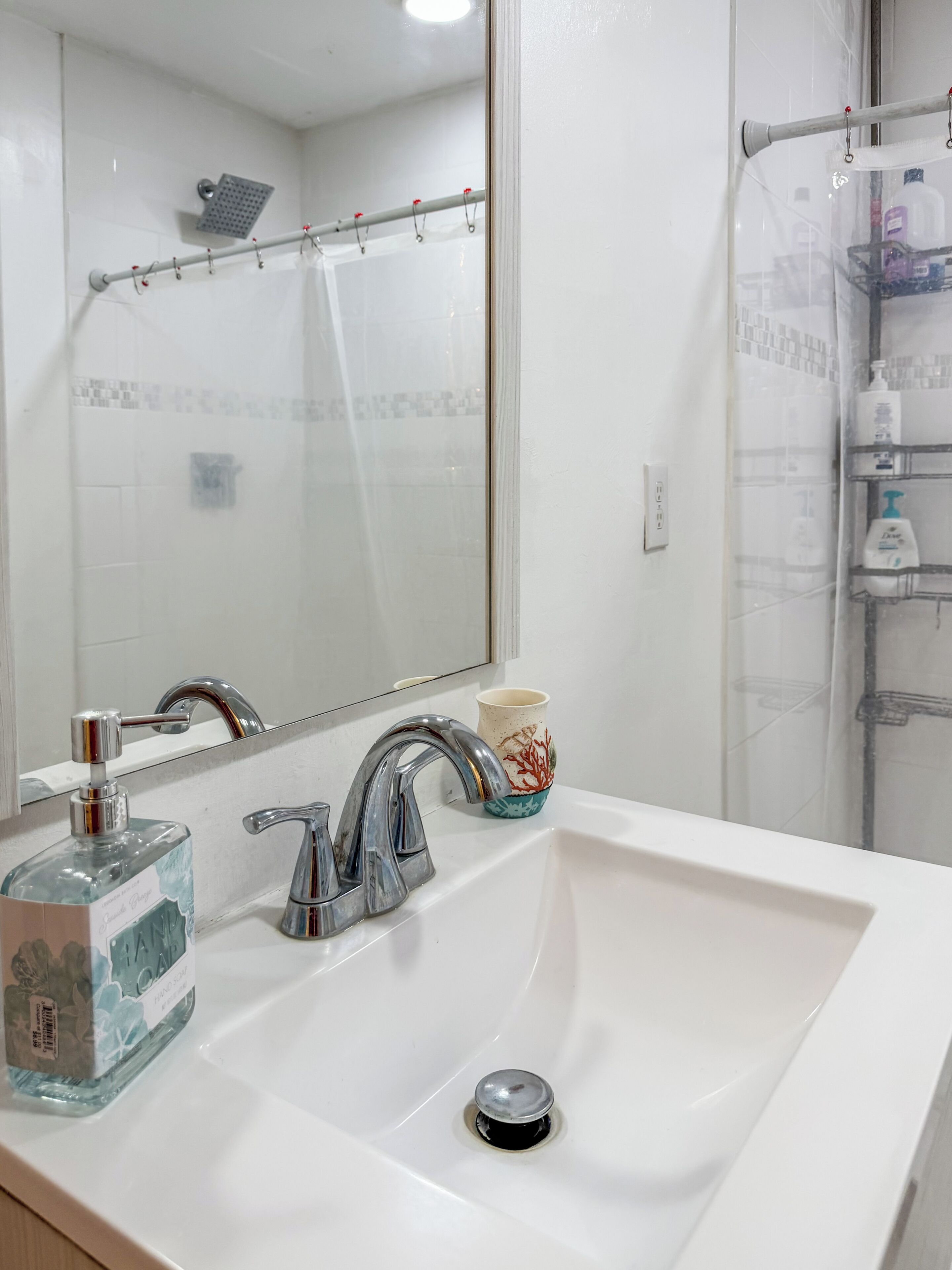 Een badkamer met een witte wastafel, een spiegel, een douche en een handdoekhouder.