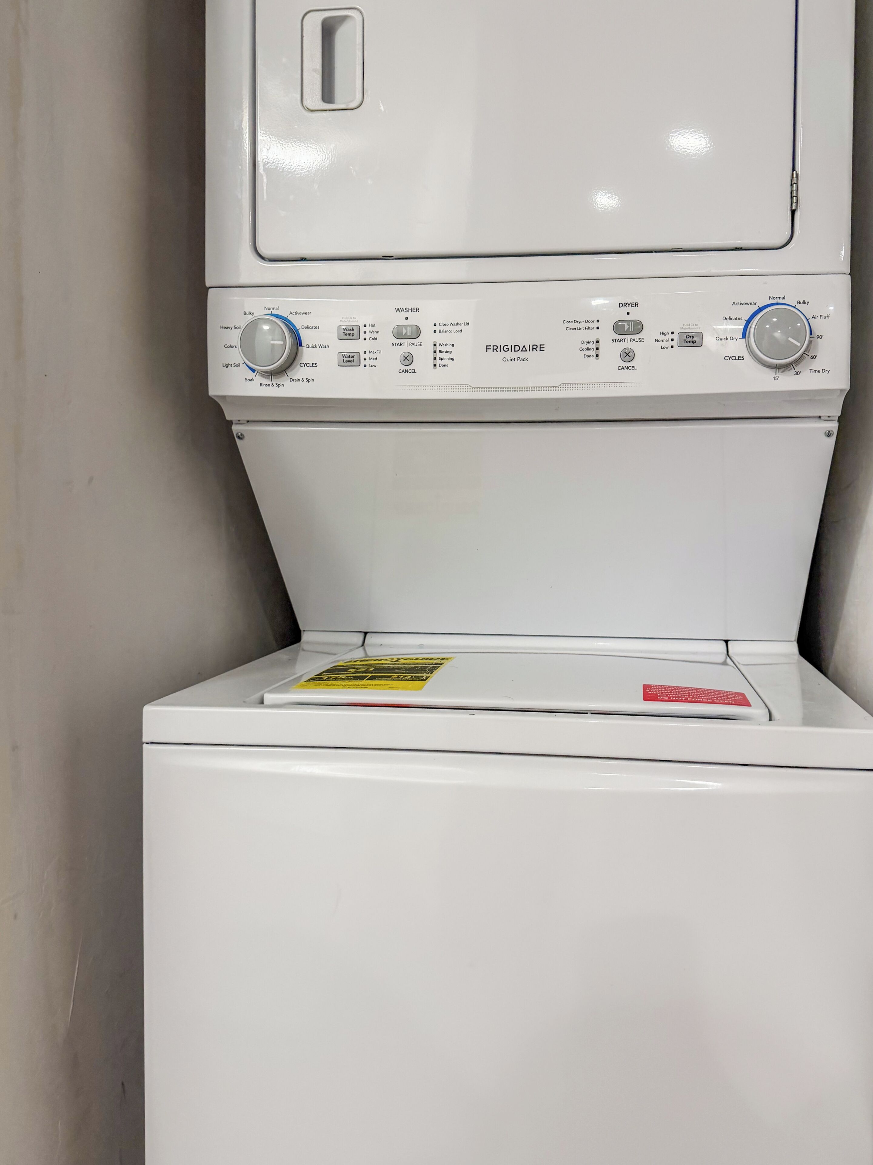 A front-loading washing machine with control panel, detergent dispenser, and a warning label.